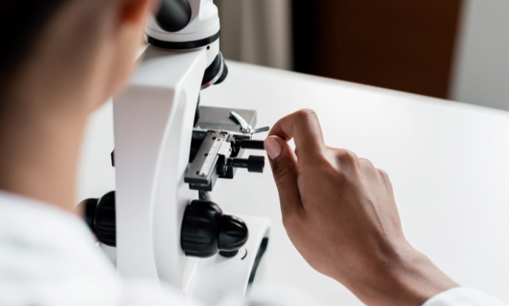 osoba patrząca przez mikroskop optyczny